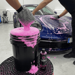 Champú de espuma rosa Refresh Cars en guante de microfibra sobre cubo, lavando un Porsche azul