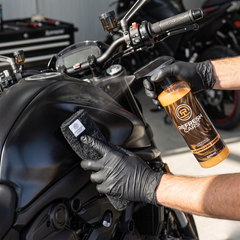 Limpiador de salpicaderos Refresh Cars pulverizado sobre el depósito de una moto con paño